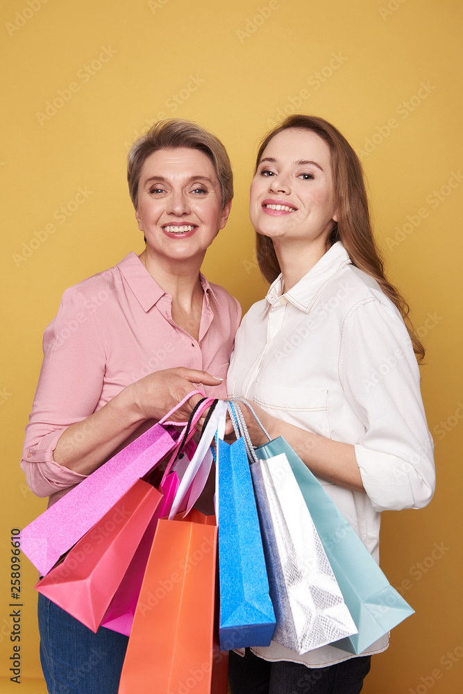 Low angle of Caucasian smiling women posing in studio with shopping bags Low angle of Caucasian smiling women posing in studio with shopping bags