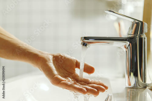 Man washing and cleaning her hand in bathroom, soft focus. Closeup of fingers under flowing tap water. Hygiene, bedtime procedures