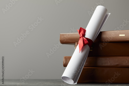 Brown books and diploma with red ribbon isolated on grey