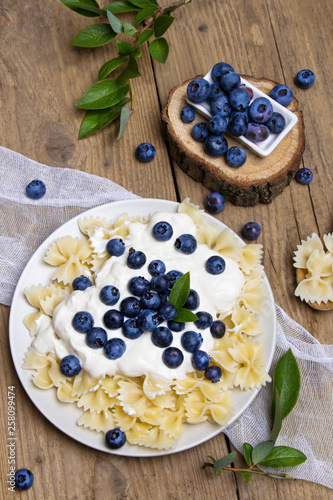 Tasty pasta with fresh organic blueberries and vanilla cream. Sweet dinner on retro wooden table.