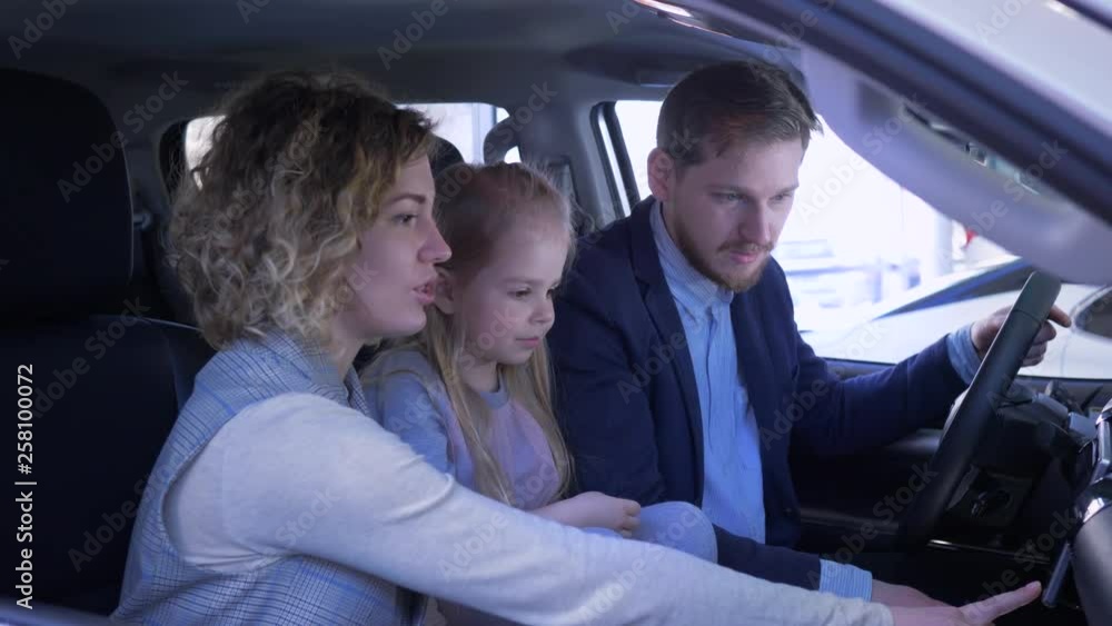 Auto business, happy smiling mom and daddy with kid girl reviews new family automobile waving key and giving thumbs up while sitting in cabin at car showroom Auto business, happy smiling mom and daddy with kid girl reviews new family automobile waving key and giving thumbs up while sitting in cabin at car showroom