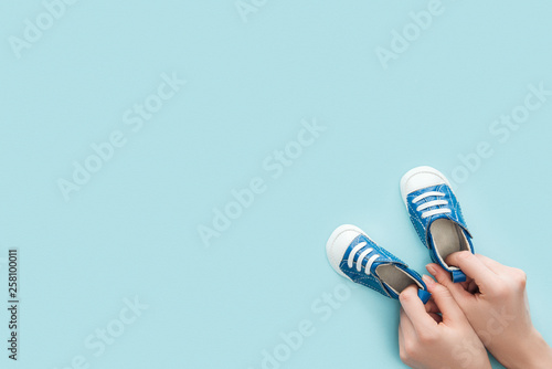 partial view of adult woman holding sneakers on blue background with copy space