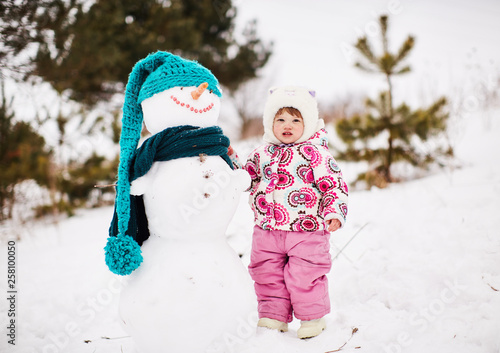 A little pretty girl is standing near a smiling snowman