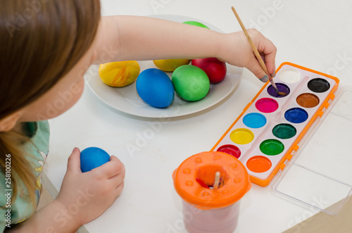 little child paints easter eggs by brush