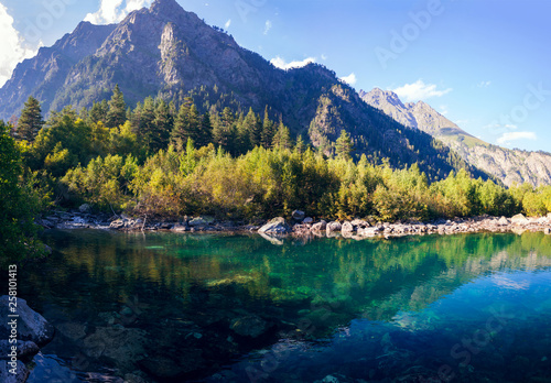 A huge panorama of the High-mountainous Baduk lake among the high Caucasian mountains and beautiful trees. Sunny summer day.