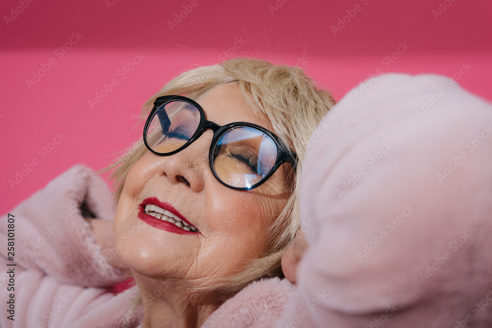 Portrait of modern elderly woman wearing eyeglasses and stretching in studio