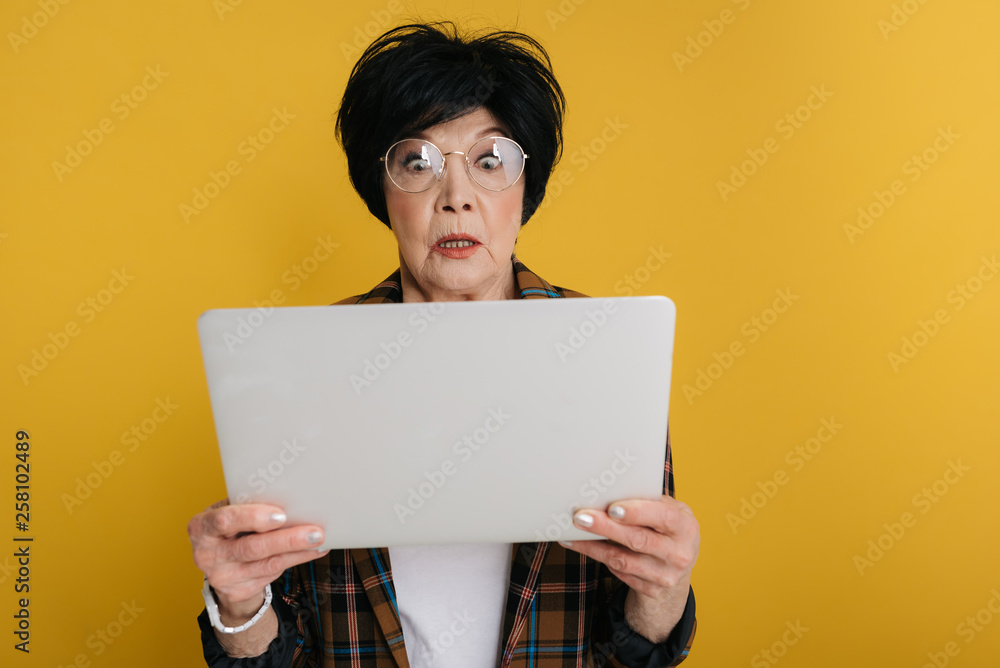Surprised elderly lady is looking at screen of computer with big eyes Surprised elderly lady is looking at screen of computer with big eyes