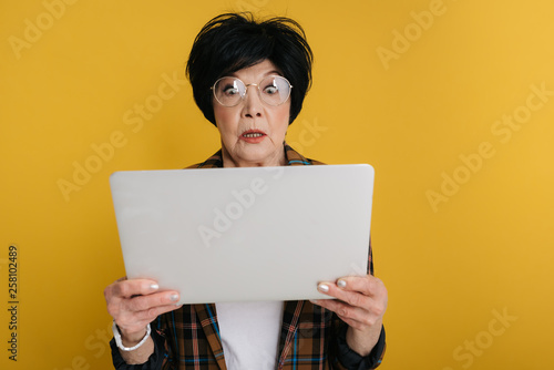 Surprised elderly lady is looking at screen of computer with big eyes