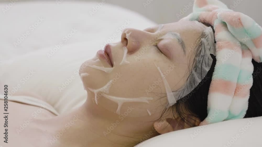 side view asian elegant woman applying facial mask on face close eyes relaxing resting lying on white bed waiting for minutes time. girl with headband and moisturizer product sleep peaceful bedroom side view asian elegant woman applying facial mask on face close eyes relaxing resting lying on white bed waiting for minutes time. girl with headband and moisturizer product sleep peaceful bedroom
