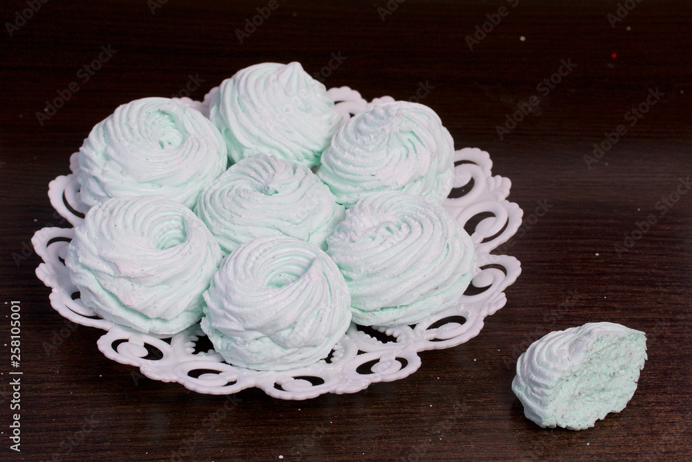 Homemade marshmallows laid on a plate. Marshmallow with mint, with a green tint. Nearby is a piece of marshmallow, its slice is visible.