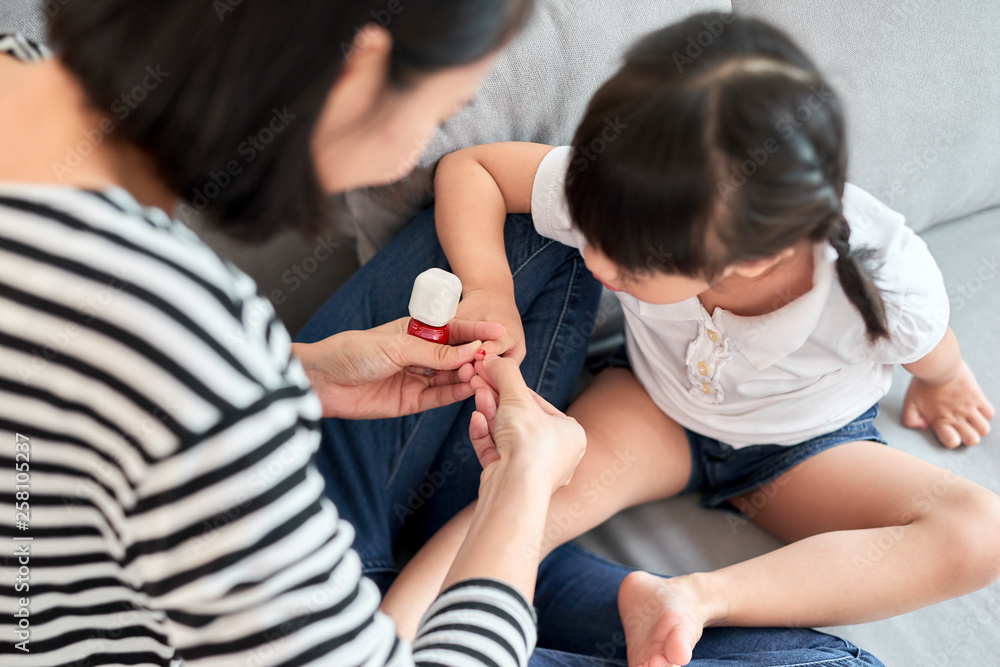 Beautiful young mother is painting the nail varnish to her cute little daughter Beautiful young mother is painting the nail varnish to her cute little daughter