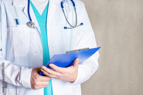A man in a white medical gown is holding a blue folder. Cropped photo of a doctor, closeup. Bright photo with space for text.