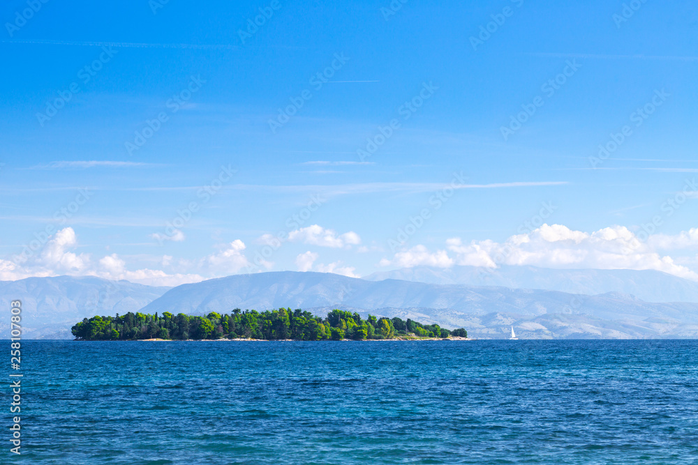 Naklejka premium Wonderful romantic summertime panoramic seascape. Sailing yacht with white sails in to the crystal clear azure sea. Small green island against coastline slopes.
