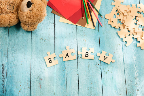 Stationery and word BABY made of letters, mock up and pieces of puzzles on wooden background. Concept of family, baby, pregnancy, maternity, parenting, children.