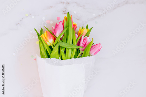Spring concept. Golden star decorations  vibrant confetti and pink and red tulips on marble background. Copy space  flat lay.