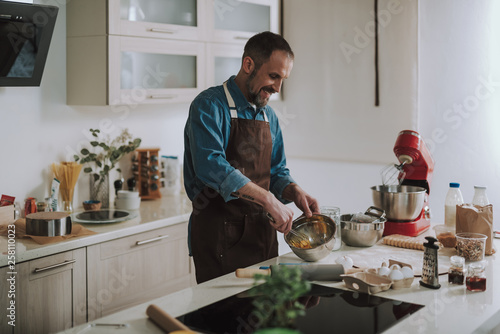 Enthusiastic man smiling while beating up eggs in bowl