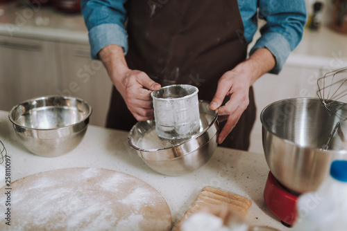 Fototapeta Naklejka Na Ścianę i Meble -  Hands of person sifting flour into deep bowl