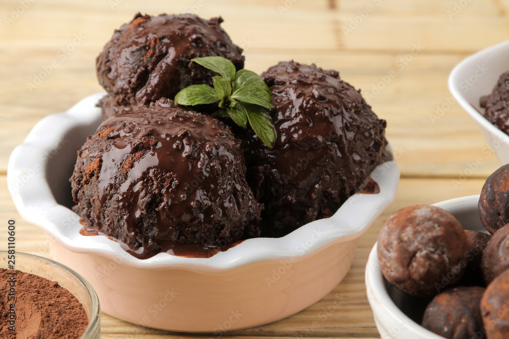Chocolate ice cream with liquid chocolate and a mint leaf on a natural wooden background. Chocolate ice cream with liquid chocolate and a mint leaf on a natural wooden background.