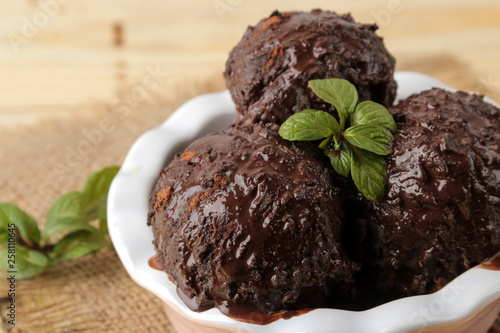 Chocolate ice cream with liquid chocolate and a mint leaf on a natural wooden background.