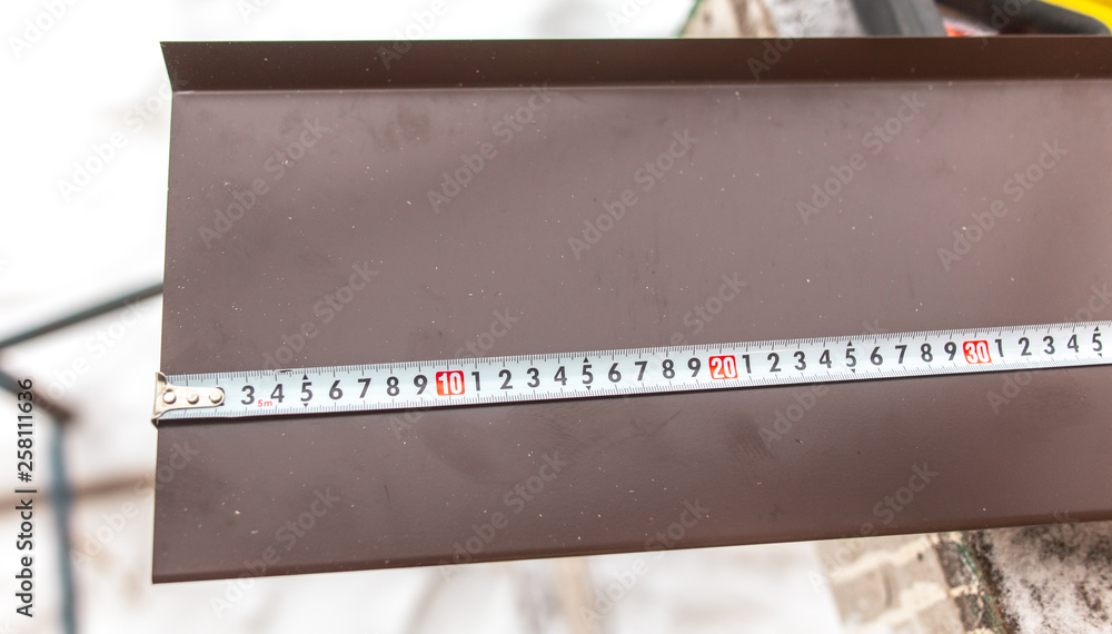 A worker measures metal at a construction site with a meter A worker measures metal at a construction site with a meter