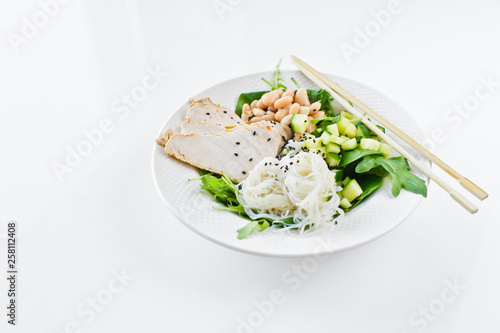 Buddha bowl with glass noodles, beans, chicken breast, spinach, arugula and cucumber. White background, side view, space for text
