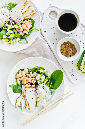 Healthy balanced food, summer restaurant menu, bowl with glass noodles, beans, chicken breast, spinach, arugula and cucumber. White background, top view