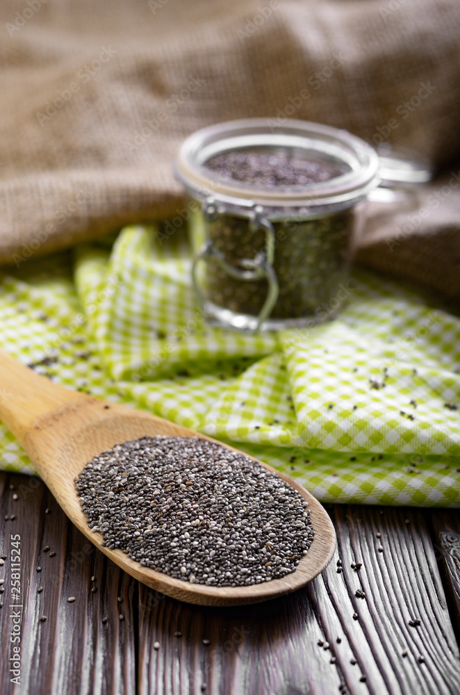 Raw Chia seeds in glass airtight jar and bamboo spatula on wooden table Raw Chia seeds in glass airtight jar and bamboo spatula on wooden table