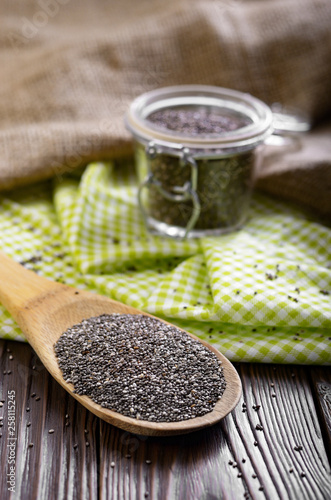 Raw Chia seeds in glass airtight jar and bamboo spatula on wooden table