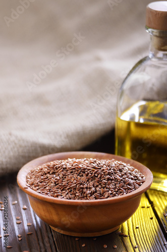 Flax oil and raw seeds in wooden bowl on kitchen table closeup