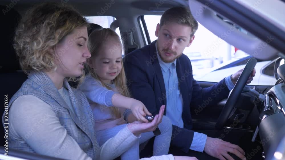 family in car sales center, merry smiling mum and dad with kid girl reviews new automobile and waving key while sitting in cabin at auto dealership family in car sales center, merry smiling mum and dad with kid girl reviews new automobile and waving key while sitting in cabin at auto dealership