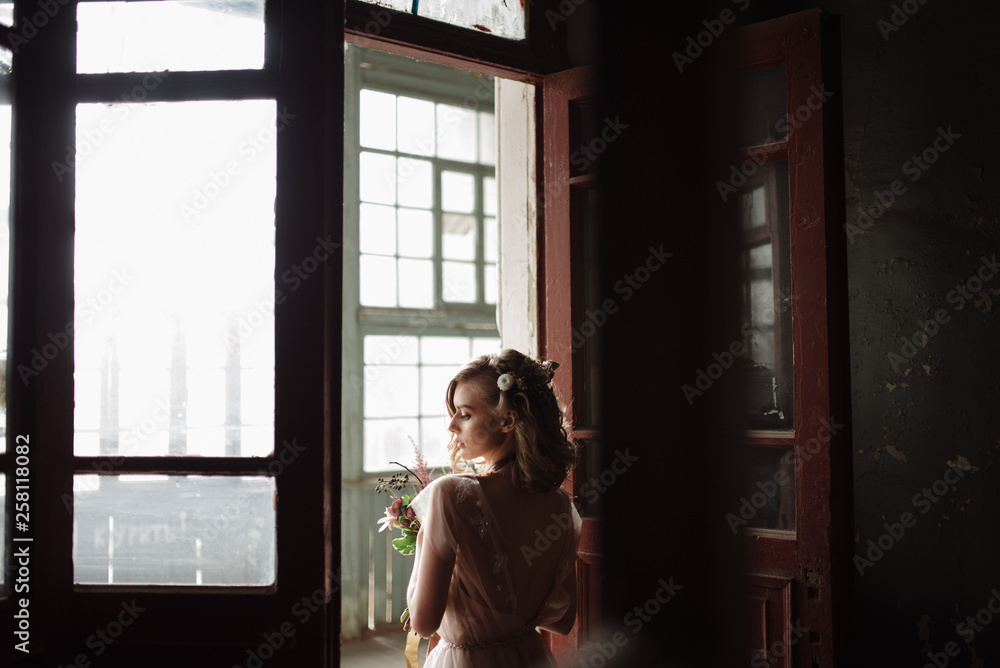 Young woman posing in a pink long dress backs indoors