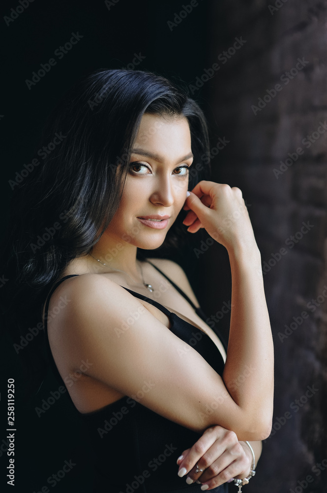 Beautiful girl in a black tight-fitting dress and heels. Black long wavy hair. Eastern appearance. Beautiful cut eyes. Brown sofa and green wall. A dark room. Sexy and stingy brunette. Portrait. Beautiful girl in a black tight-fitting dress and heels. Black long wavy hair. Eastern appearance. Beautiful cut eyes. Brown sofa and green wall. A dark room. Sexy and stingy brunette. Portrait.