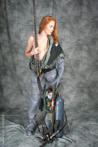 Nude young woman with red hair and freckles with a chain in her hands in a vintage diving suit.