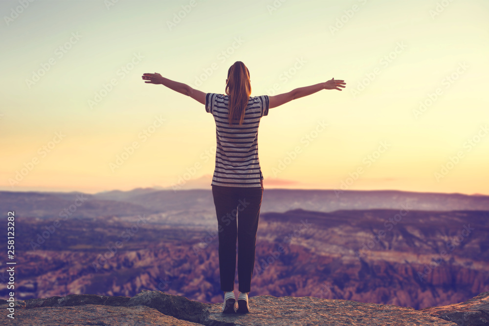 The girl at the top of the mountain alone, admires the beautiful view of the natural landscape and raises her hands up.