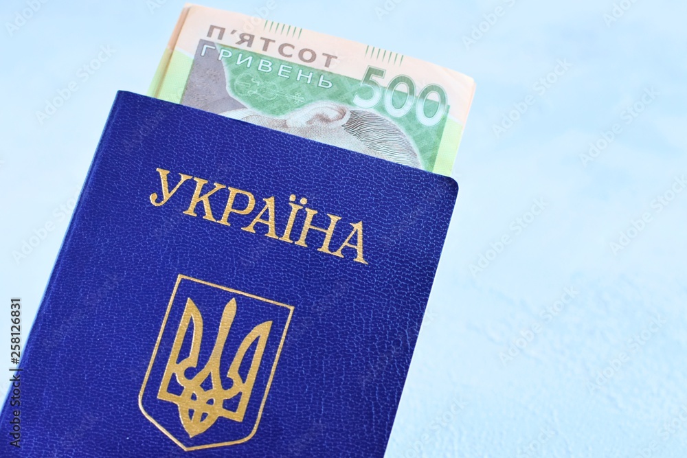 Fototapeta premium Internal passport of Ukraine with the national currency hryvnia inside on neutral background. Passport of a citizen of Ukraine with a state emblem trident on the blue cover and money inside 