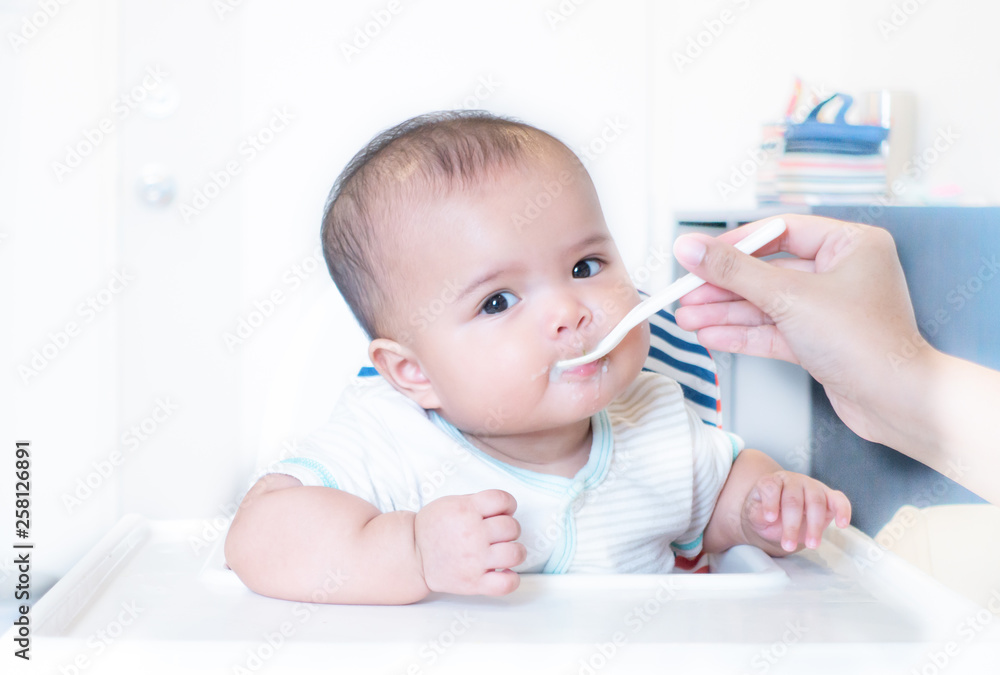 Mother feeding baby food on high chair Mother feeding baby food on high chair