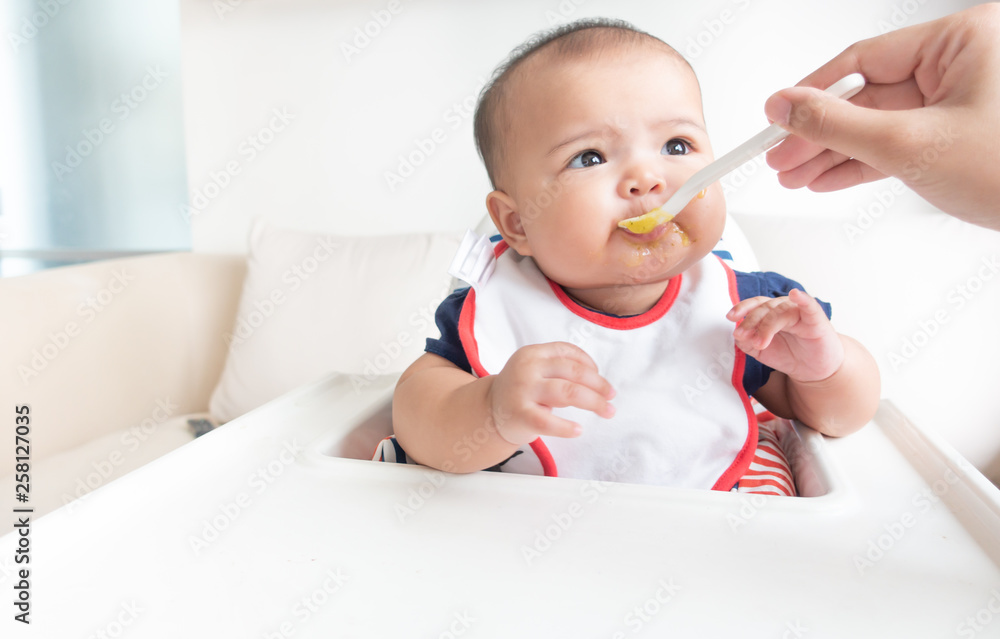 Mother feeding baby food on high chair Mother feeding baby food on high chair