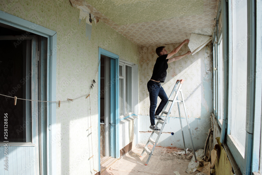 man removes old wallpaper from the ceiling