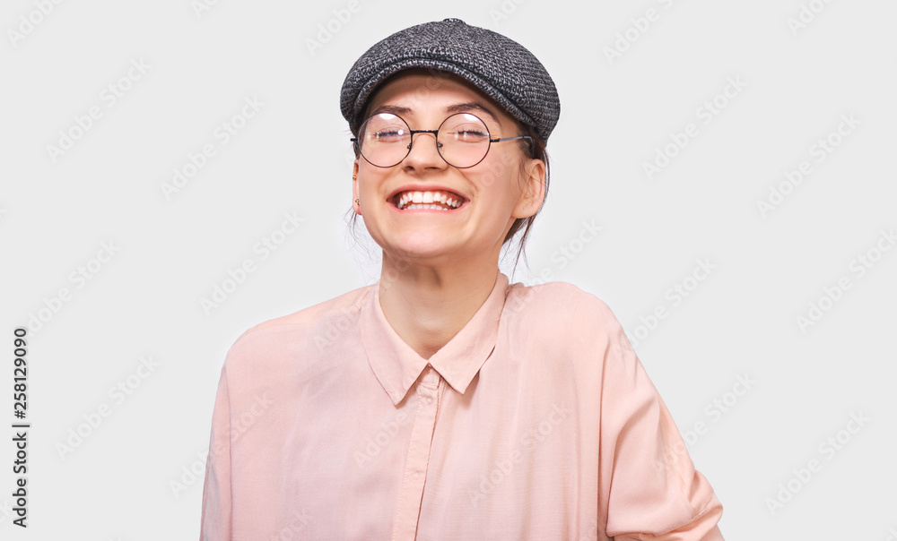 Candid shot of happy young woman, smiling broadly, wears pink shirt and round transparent spectacles. Pretty girl student feels joyful and posing over white studio wall. People and emotions concept Candid shot of happy young woman, smiling broadly, wears pink shirt and round transparent spectacles. Pretty girl student feels joyful and posing over white studio wall. People and emotions concept