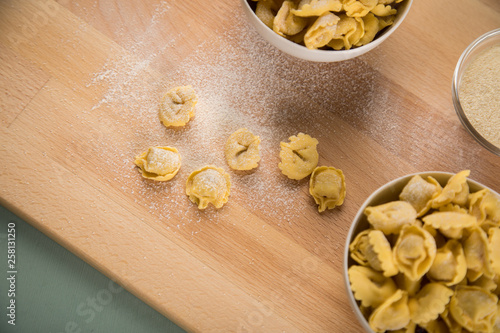 Frische, rohe Cappelletti Tortellini Pasta mit Mehl und Grieß in Porzellan Schale auf Holz Brett und Pastell Grün Hintergrund