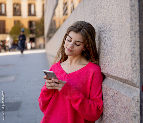 Attractive young woman on smart phone checking social media mobile apps outside in an European city