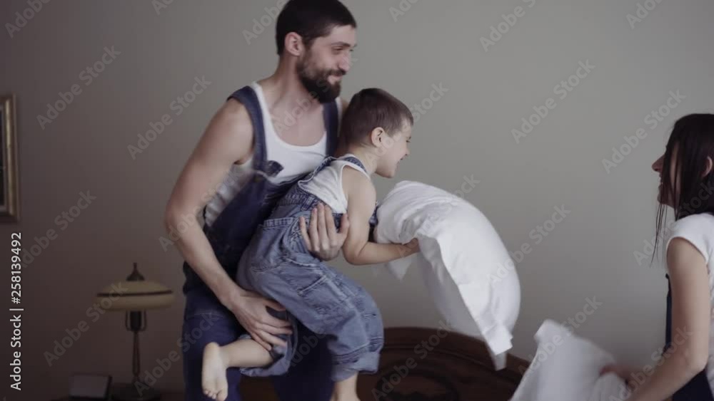 Happy family playing with pillows together on bed. Parents spending free time with their son. Happy family playing with pillows together on bed. Parents spending free time with their son.