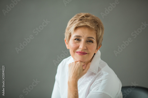 portrait of a stylish old woman with a short haircut in a white shirt on a gray background