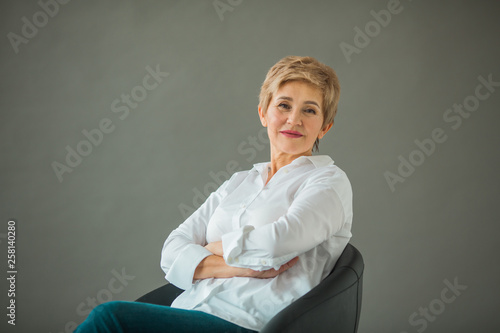 Foto portrait of a stylish old woman with a short haircut in a white shirt on a gray