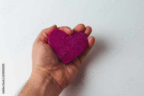 Hand holding a pink heart shape over white background