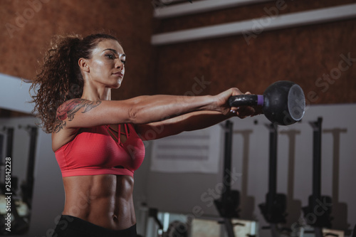 Attractive female crossfit athlete working out with kettlebell at the gym. Beautiful sportswoman with perfect fit body lifting kettlebell at crossfit box gym