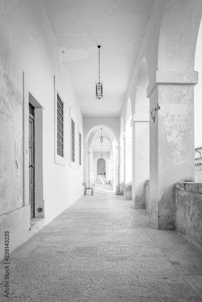 A long corridor under an arcade, with the light passing through the arches and columns. Cross vault. A long corridor under an arcade, with the light passing through the arches and columns. Cross vault.