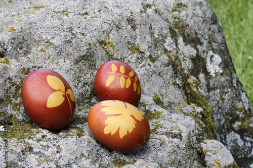 Trois oeufs de Pâques décorés de feuilles sur un rocher dans la nature. / Three Easter eggs decorated with leaves on a rock in nature. 