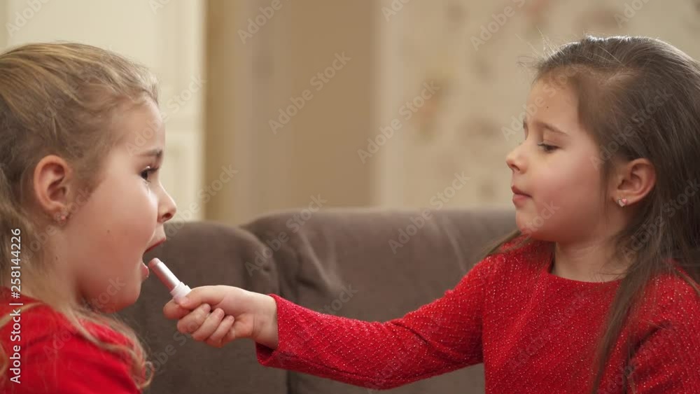 Little girl playing with lipstick and applying it to her friend Little girl playing with lipstick and applying it to her friend