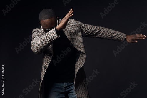 Serious cool man in black sweater and brown plaid coat and jeans. Studio, dark key